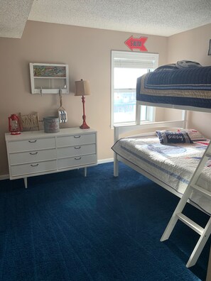 Un dormitorio con literas, un aparador, un mapa, una lámpara y una ventana.
