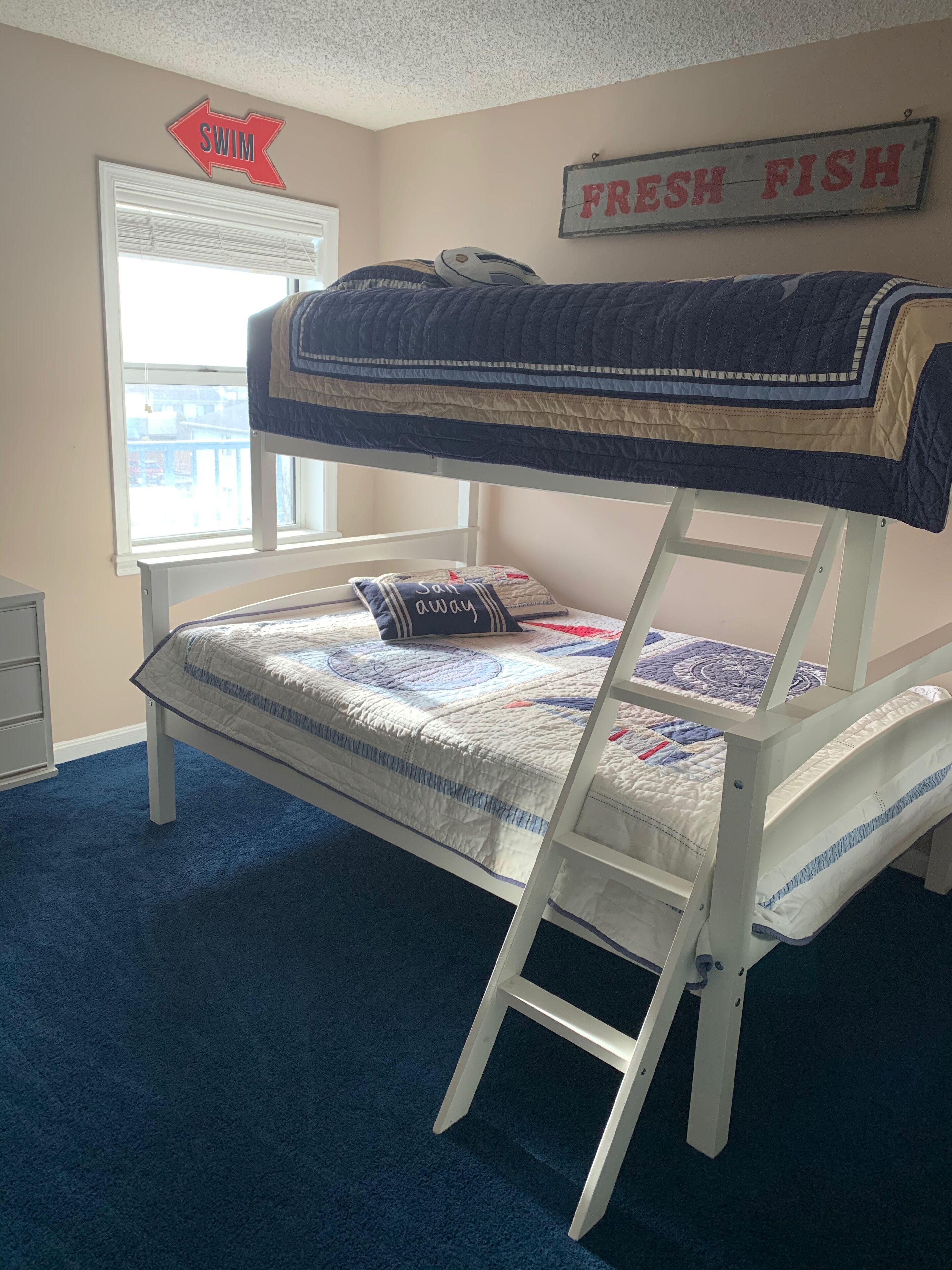 A bunk bed with a ladder, a window with blinds, and a wall sign that reads "SWIM FRESH FISH".