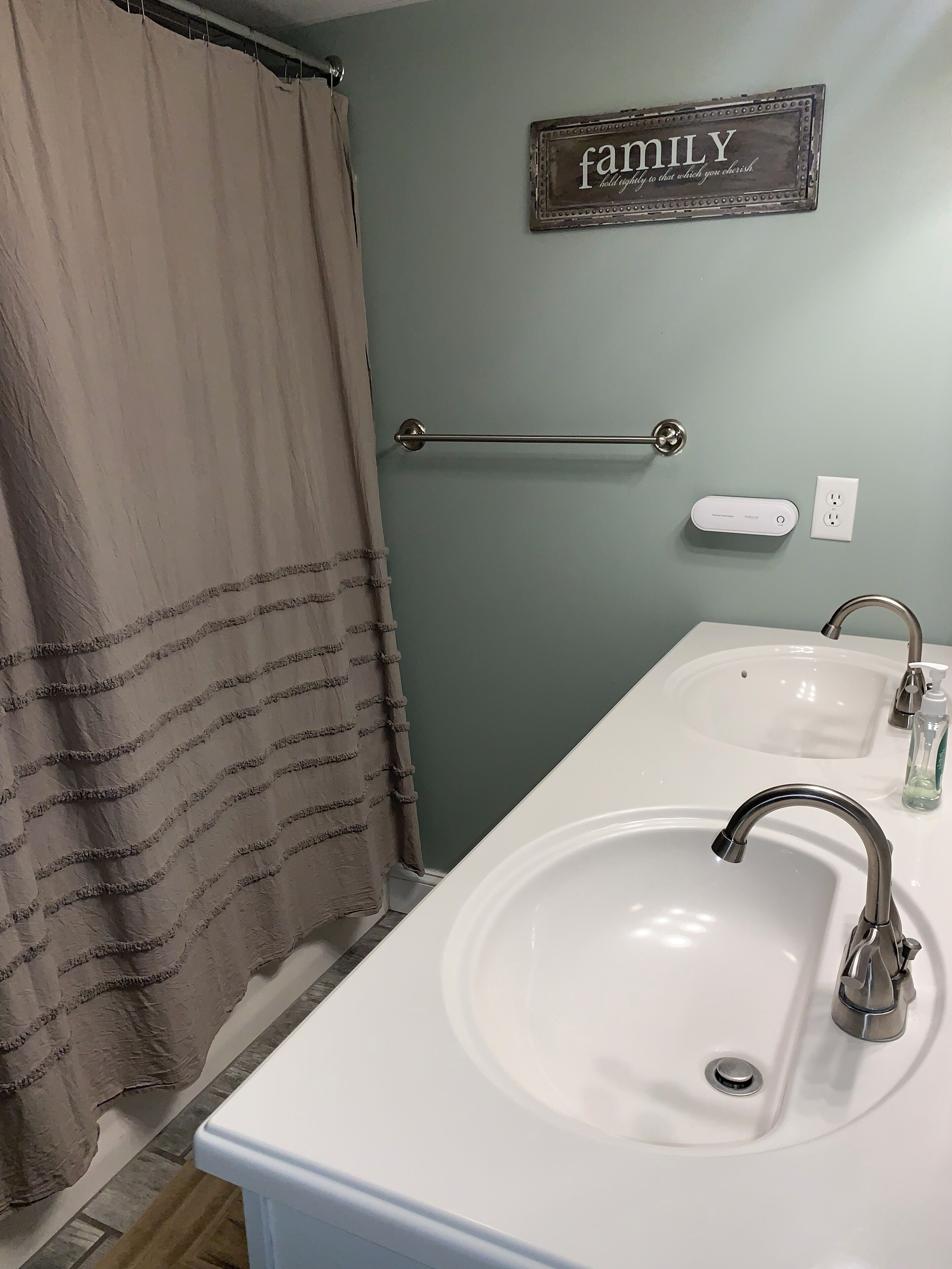A bathroom with a white sink, a mirror, a towel rack, a shower curtain, and a 'family' sign on the wall.