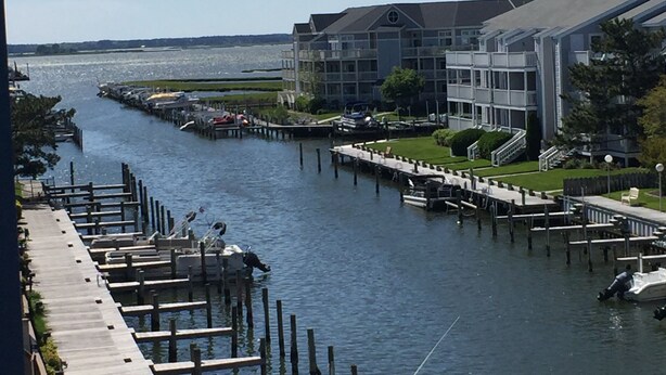 A marina with docked boats, a wooden walkway along the water, and a building with a grey facade.