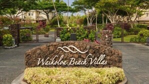 Waikoloa Beach Villas -nimelle varustettu kyltti, jonka edessä on kivimuuri ja maisemoitu puutarha.
