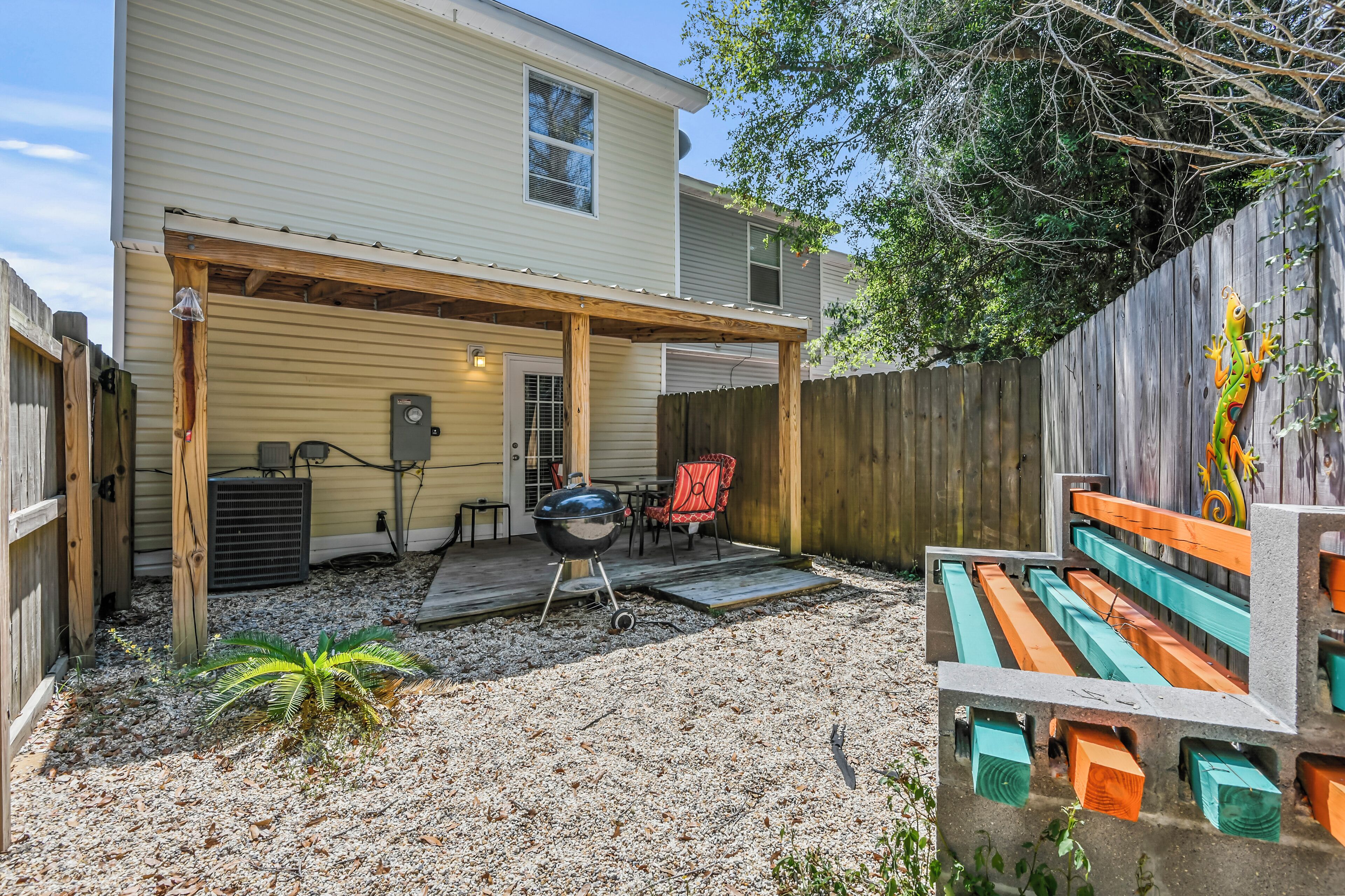 Een achtertuin met een overdekt terras, een barbecue, tuinmeubels en een houten omheining.