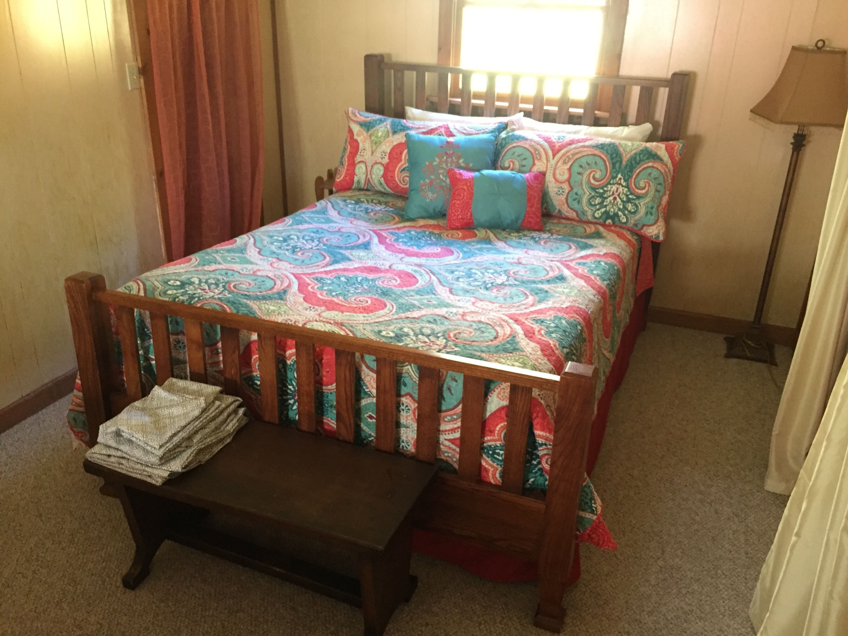 A bedroom with a wooden bed, colorful bedding, a bedside table, and a lamp.