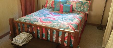 A bedroom with a wooden bed, colorful bedding, a bedside table, and a lamp.