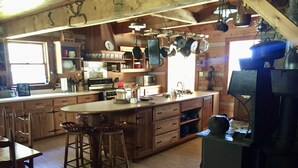 A rustic kitchen with wooden cabinets, a central island, and hanging pots. - Simply Irresistible: Authentic Log Cabin (Creston)
