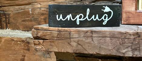 A rustic wooden sign with the word "unplug" and a plug icon, placed on a stone ledge against a wooden wall.