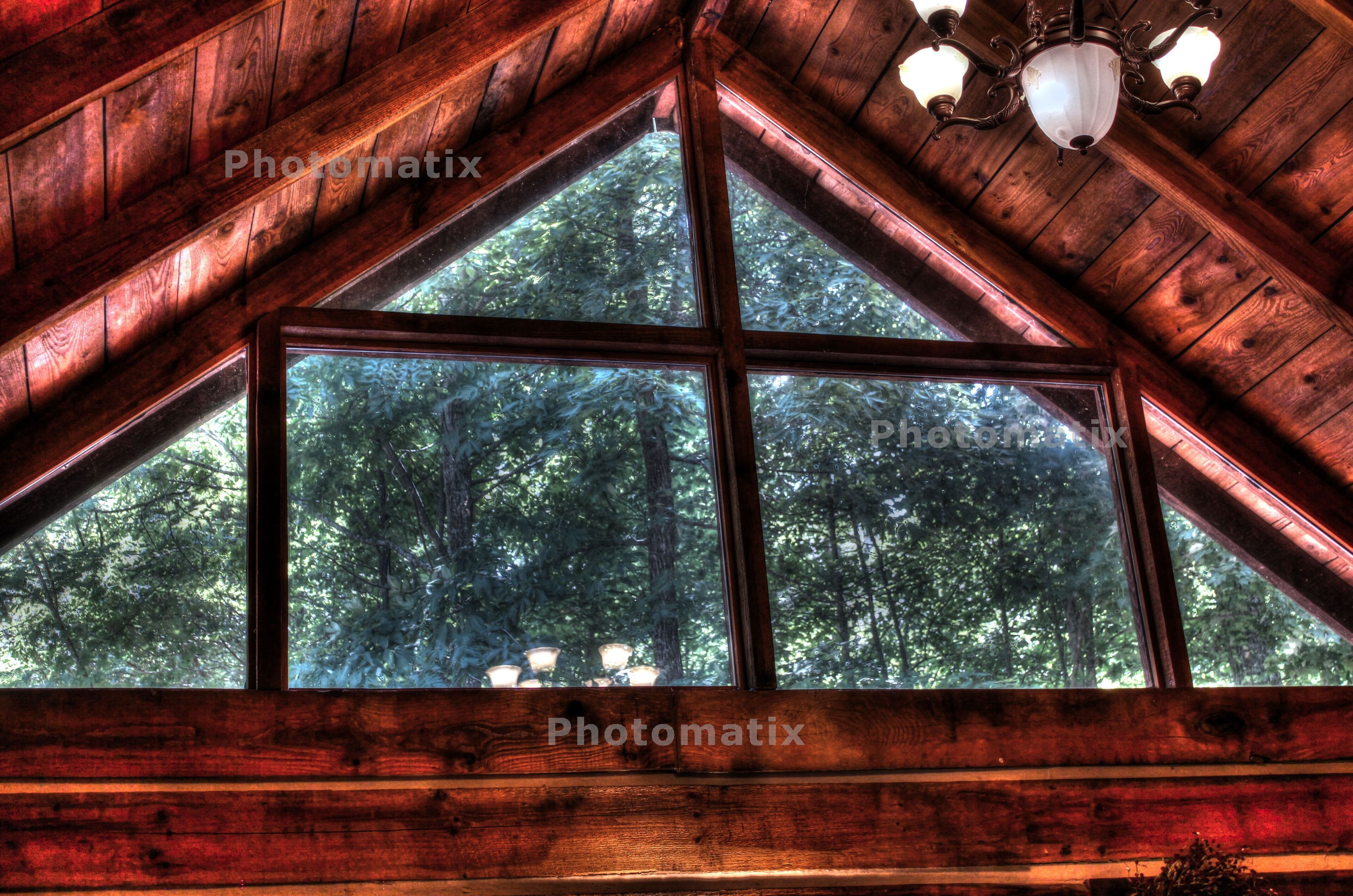 Une cabane en bois dotée d’une grande fenêtre triangulaire qui offre une vue sur une forêt.