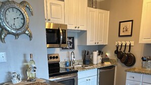 A kitchen with white cabinets, a microwave, a stove, and a clock on the wall.