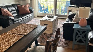 A living room with a sofa, coffee table, TV, and a balcony with chairs.