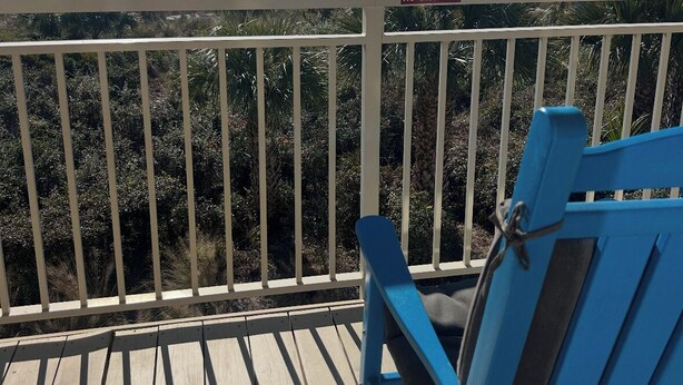 A balcony with a view of the ocean, a sign prohibiting grilling, towels on railings, and smoking.