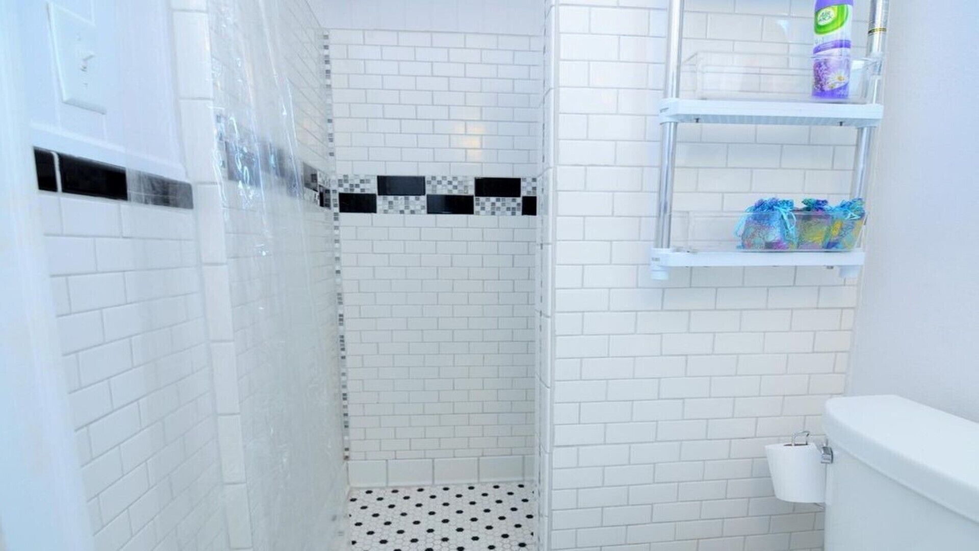 A bathroom with white subway tiles, a black and white checkered accent wall, a shower with a perforated floor, and a toilet with a paper towel holder.