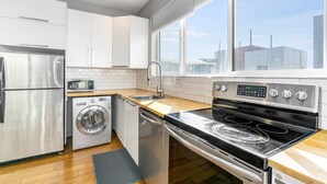 Une cuisine moderne équipée d’appareils électroménagers en acier inoxydable, d’un lave-vaisselle et d’une grande fenêtre offrant une vue sur la ville.