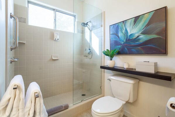 Un baño moderno con cabina de ducha de vidrio, inodoro y una obra de arte colgada.