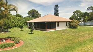 A single-story house with a covered porch, surrounded by a grassy yard and trees.