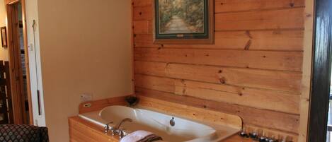 Une salle de bain rustique, avec des murs en bois, une grande baignoire, un banc en bois et un tableau encadré accroché au mur.