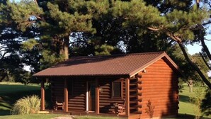 Une cabane en rondins avec une véranda et un petit jardin devant.
