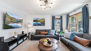 Un salon moderne avec un téléviseur à écran plat, un canapé, une table basse et des œuvres d’art accrochées aux murs.