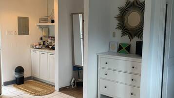 A clean, well-lit room with a bed, a dresser, a mirror, and a sunburst wall decoration.