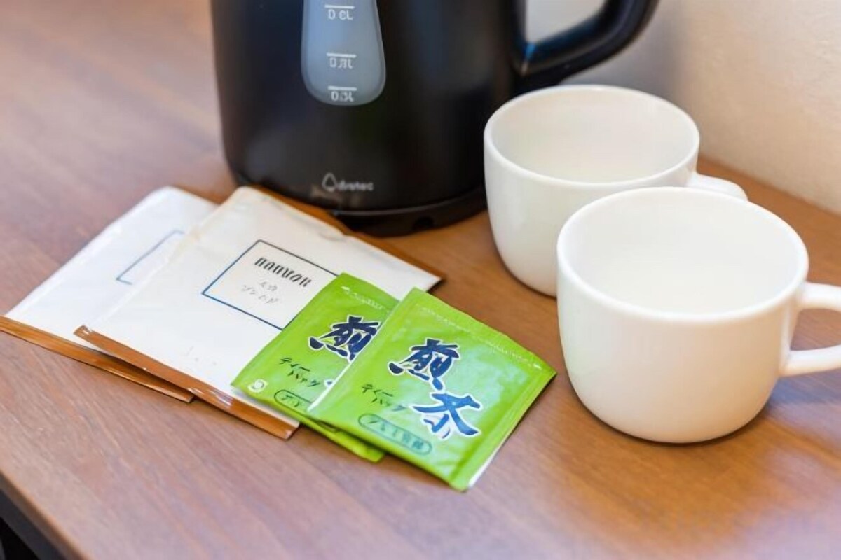 A table with a black coffee maker, two white cups, and two green packets of tea.