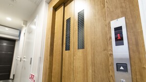 Een lift met een digitaal scherm waarop het nummer 1 staat, houten deuren en een metalen paneel met een knop.