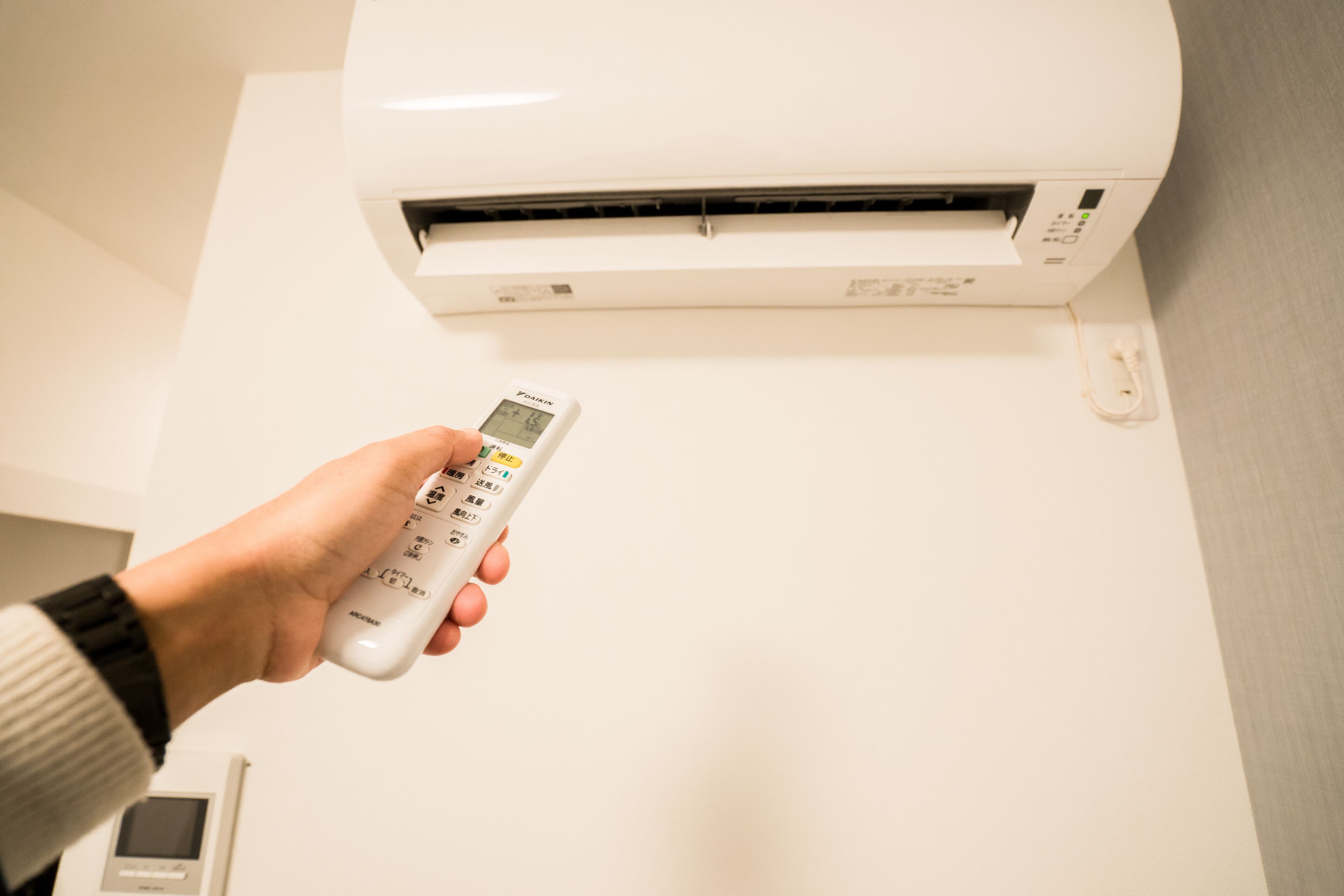 Une main tenant une télécommande devant un climatiseur fixé au mur.