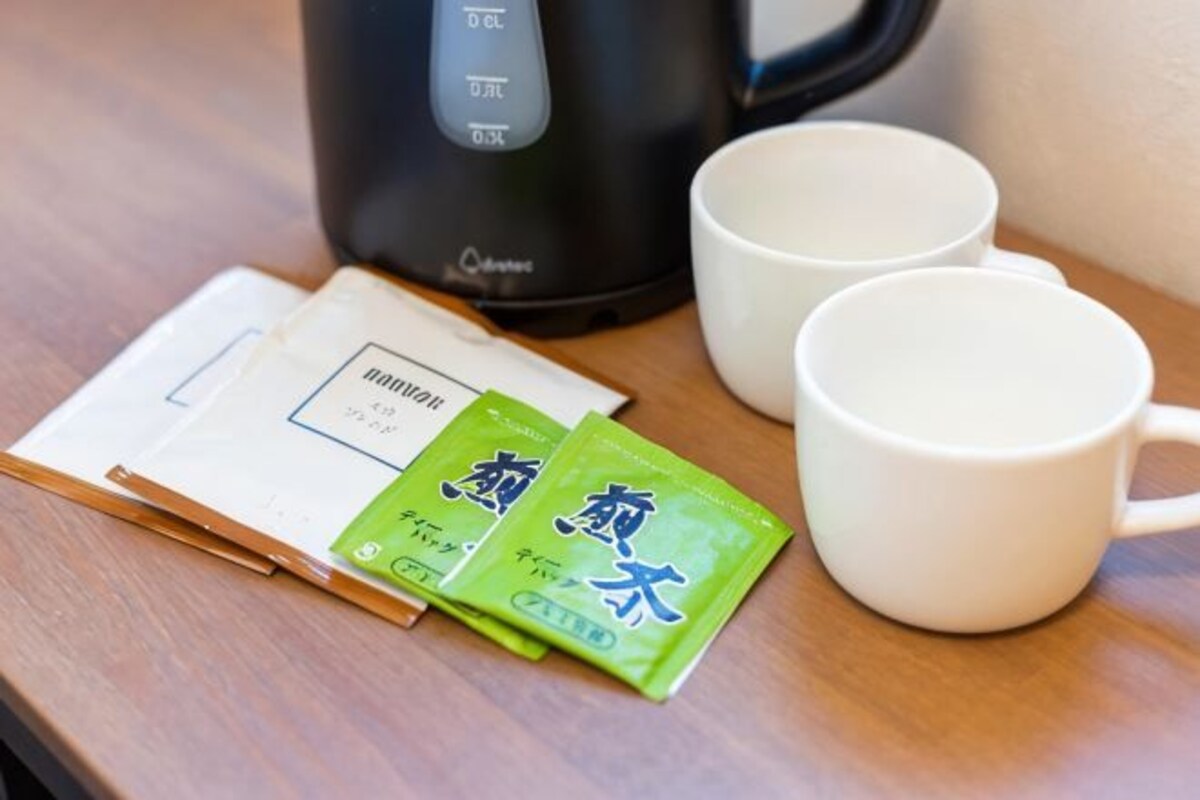 A table with a black coffee maker, two white cups, and two green packets of tea.