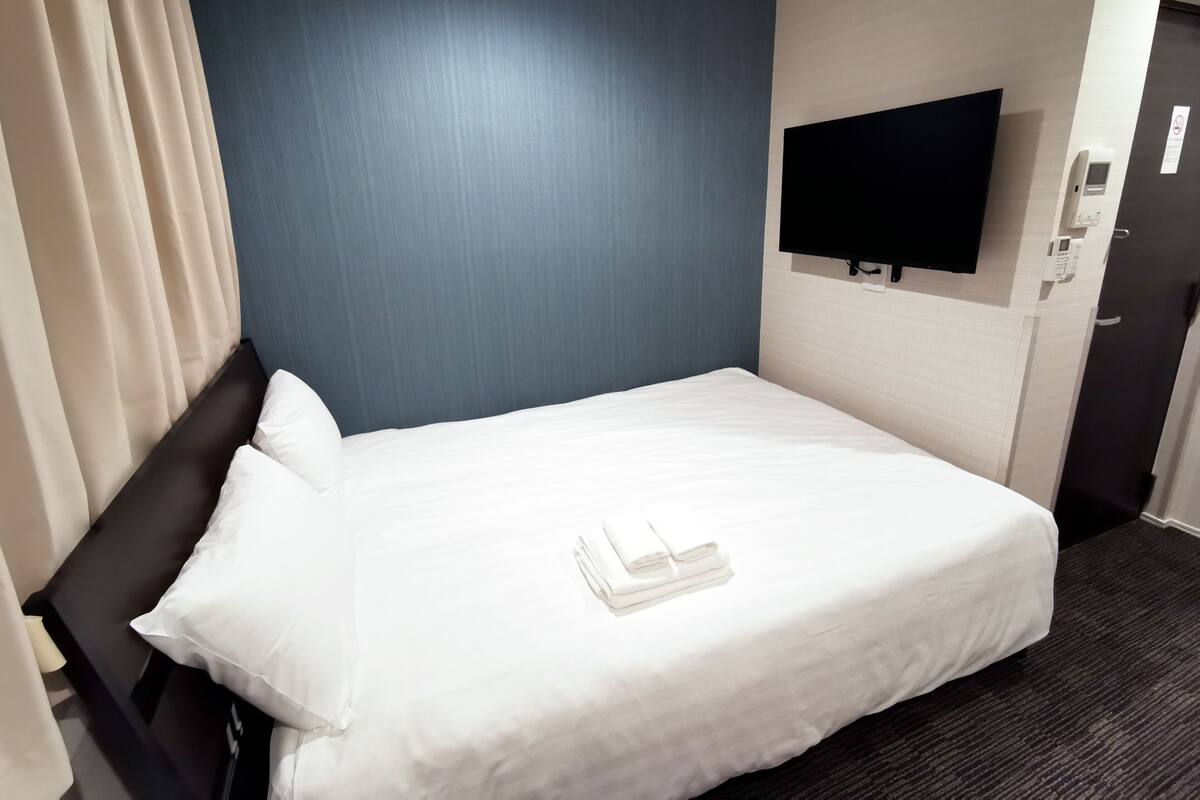 A hotel room with a bed, a flat-screen TV mounted on the wall, and a door with a phone and light switch.