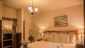 A bedroom with a large bed, bedside lamps, a nightstand, a mirror, and a painting on the wall. - Hotel Mansion del Rey (Antigua Guatemala)