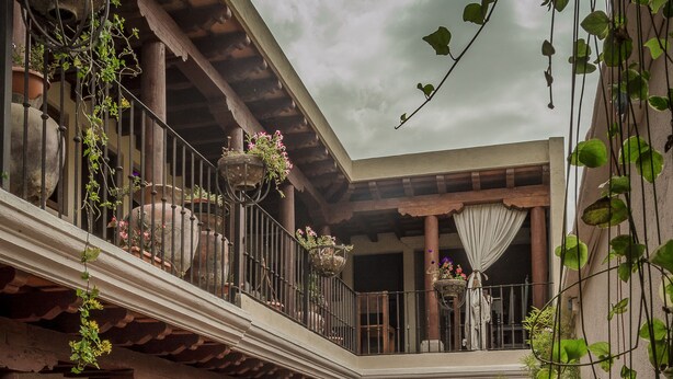 A courtyard with a tiled floor, columns, and potted plants. - Hotel Mansion del Rey (Antigua Guatemala)