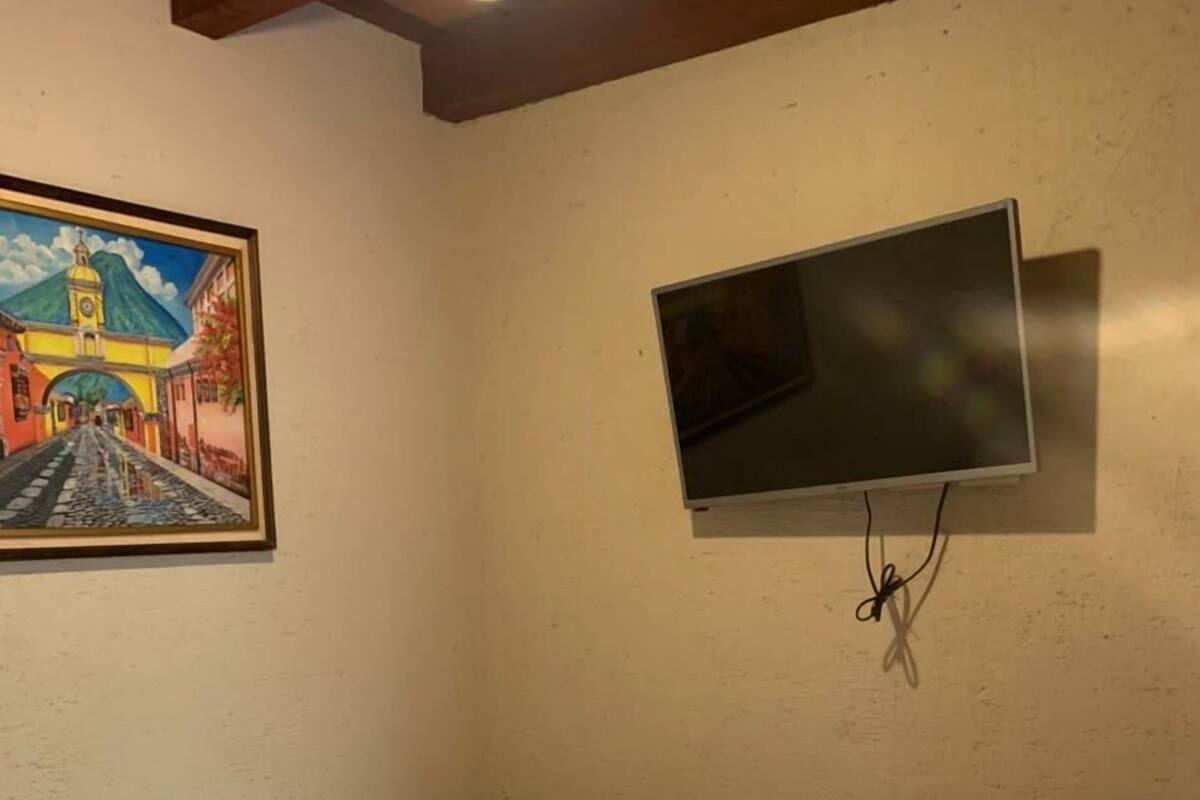 Habitación de hotel con cama, un cuadro de una escena callejera y un televisor montado en la pared.