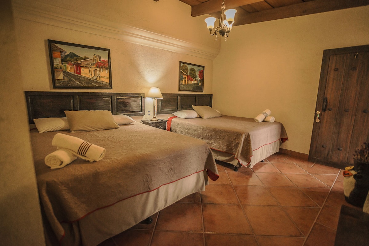Una habitación de hotel con dos camas, una puerta de madera y dos cuadros en la pared.