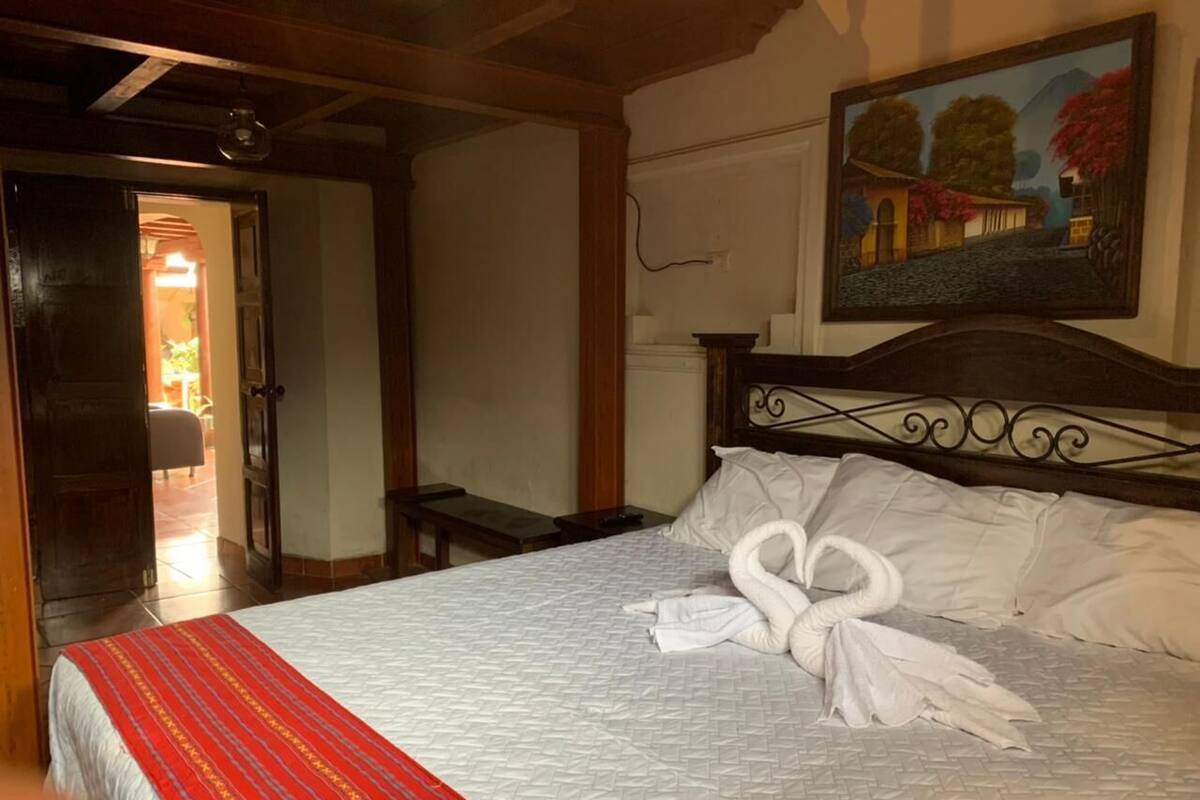 Una habitación de hotel con una cama, un cuadro en la pared y una puerta que da a otra habitación.