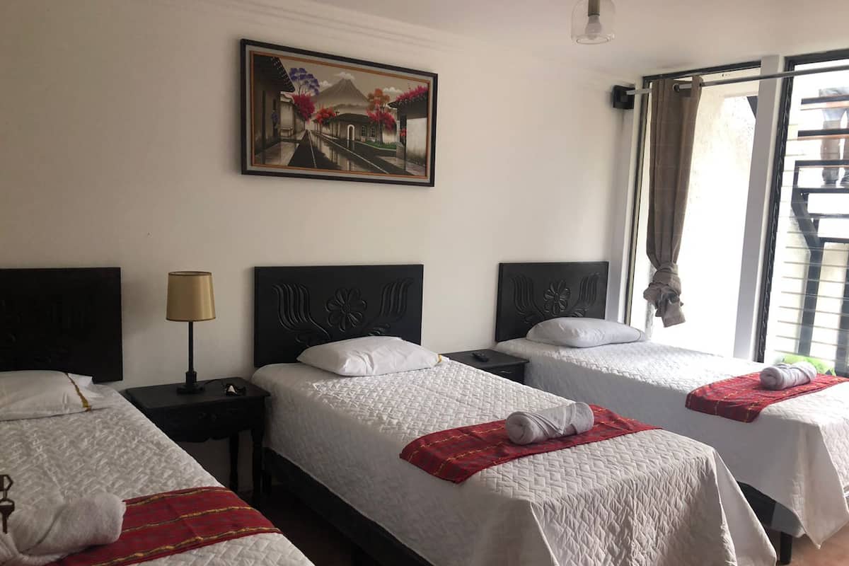 Una habitación de hotel con tres camas, un cuadro, una lámpara y una ventana con cortinas.