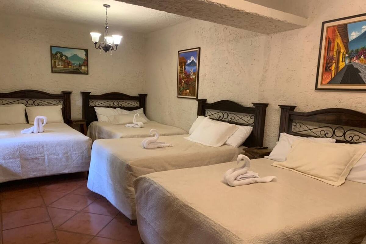 Habitación de hotel con tres camas, cada una con cubrecama y almohadas blancas, y toallas decorativas con forma de cisne.