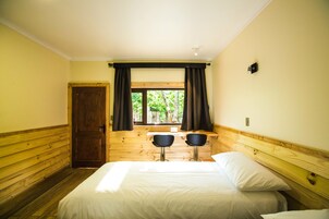 Una habitación con una cama, dos sillas, una ventana con cortinas y una puerta de madera.