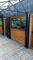 Una terraza de madera con estructura metálica y grandes ventanales.