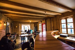 Un interior de madera con una barra curva y mesas, un área de cocina visible y un ventanal con cortinas.