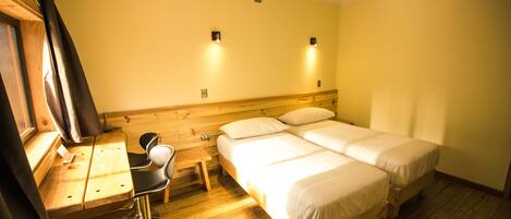 Habitación de hotel con un escritorio de madera, dos camas individuales, una silla y una mesita.