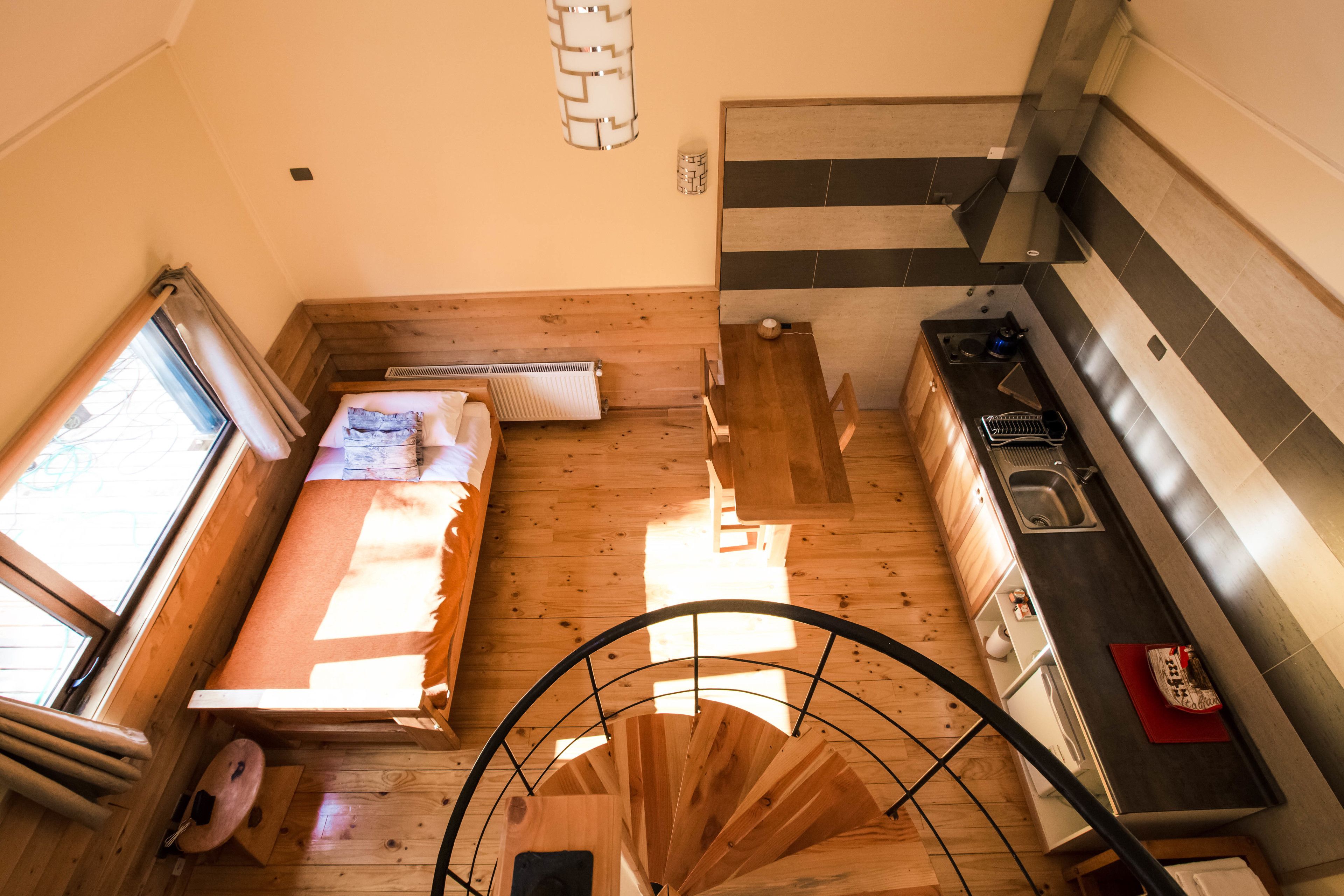 A compact room with a bed, a small kitchen area, and a spiral staircase.