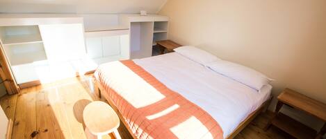 Une chambre à coucher avec un lit, un plancher en bois, un bureau et une chaise.