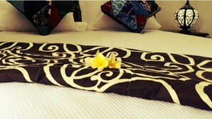 A bed with a black and white patterned bedspread, a yellow flower, and decorative pillows. - Pondok Ayu Homestay (Ubud)