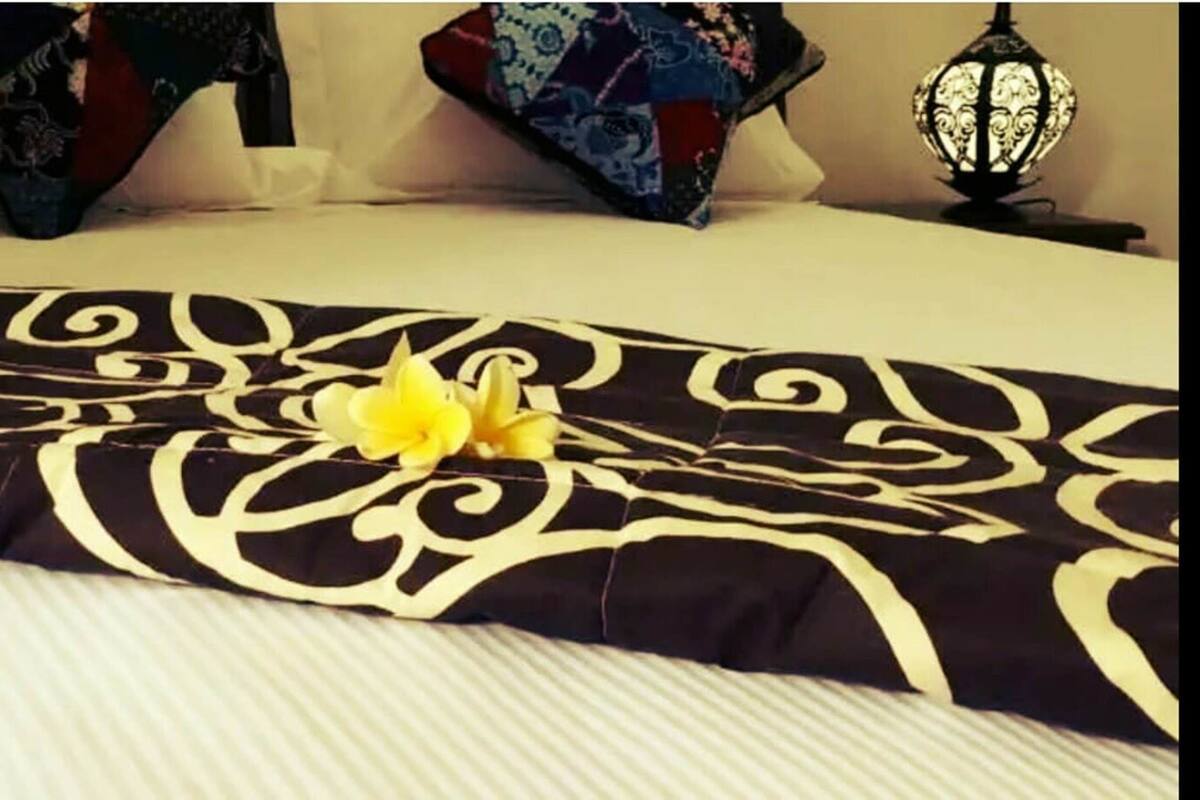 Een bed met een zwart-wit gebed en een gele bloem, plus decoratieve kussens.