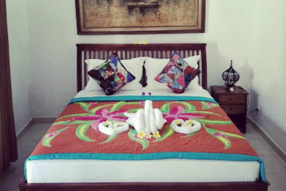 Een slaapkamer met een groot bed, een nachtkastje, een lamp en een schilderij aan de muur.
