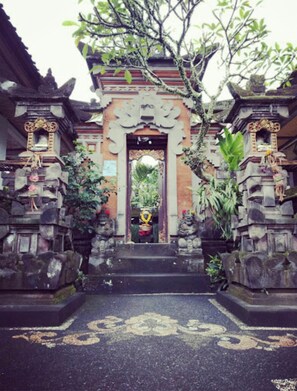 A traditional gate with intricate carvings, leading to a building with a tiled entrance. - Pondok Ayu Homestay (Ubud)
