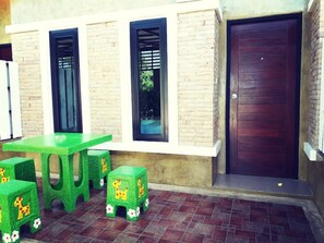 A patio area with a green table and matching stools, a dark wooden door, and windows with black frames. - Oasis Resort (Pranburi)