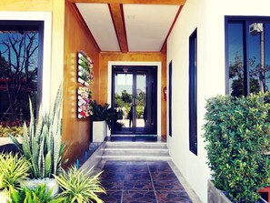 A modern building entrance with a tiled floor, a wooden ceiling, and a glass door leading to a garden. - Oasis Resort (Pranburi)