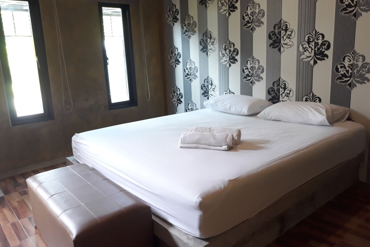 A neatly made bed with white linens and pillows, a brown bench, and a window with curtains.