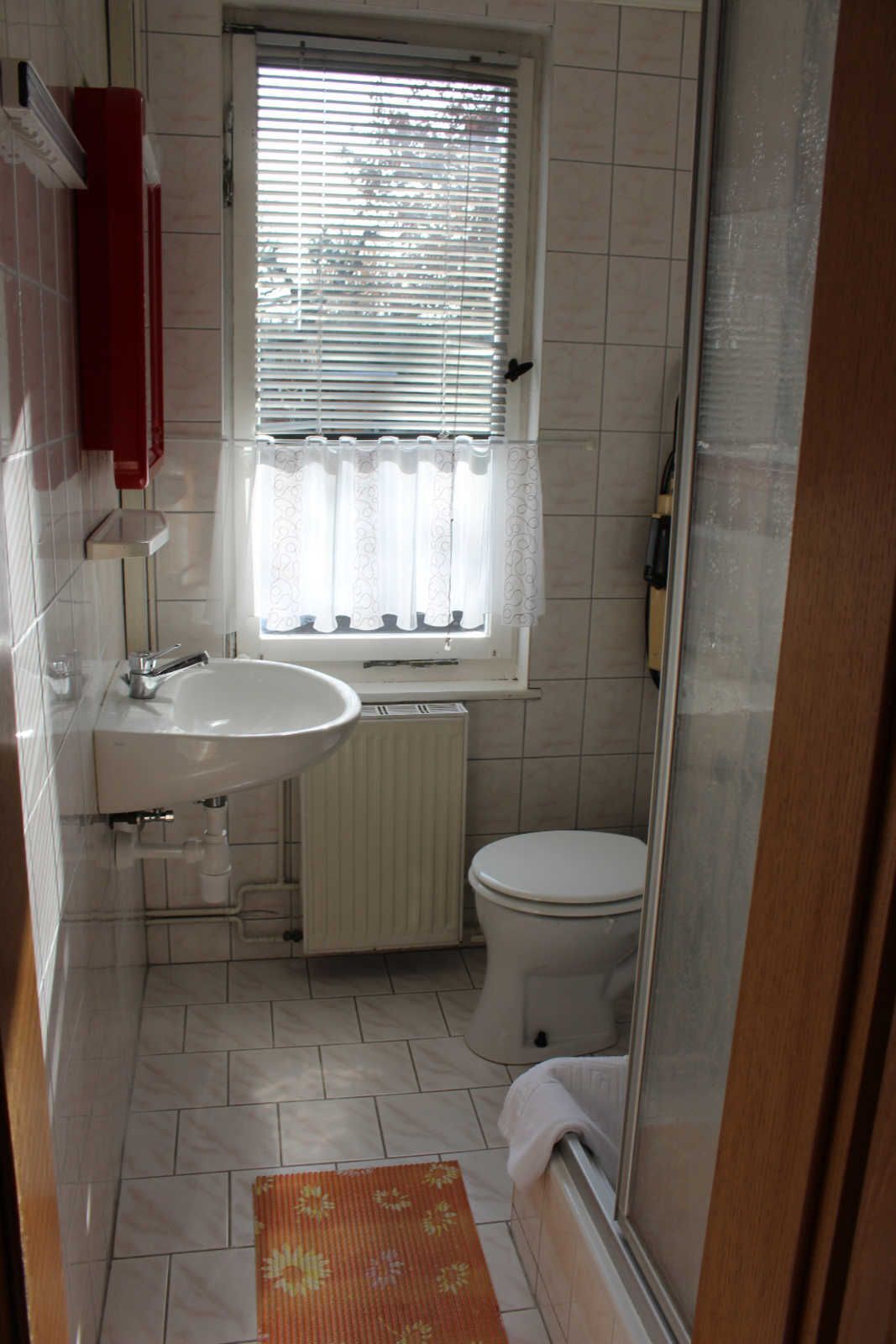A compact bathroom with a white sink, toilet, and a window with blinds.