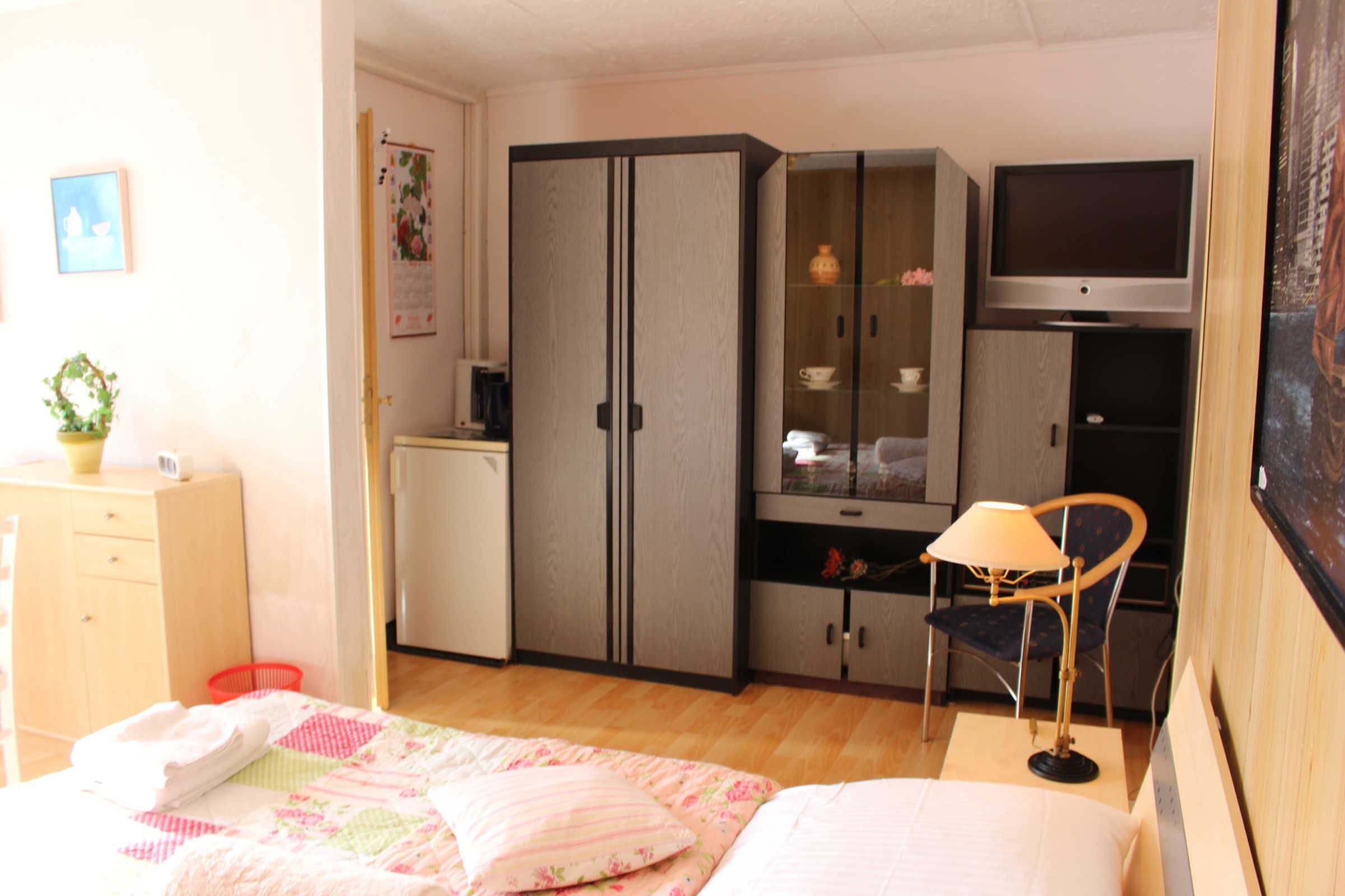 Un dormitorio con cama, armario, televisión y escritorio con silla.