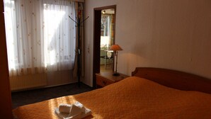 Een hotelkamer met een bed, nachtkastje, lamp, raam met gordijnen en een radiator.